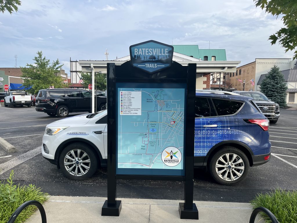 Batesville Main Street trail map sign in parking lot with cars and buildings in background.